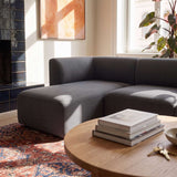 Dunkelgraues sackit Fjord Sofa mit linker Chaise in einem hellen skandinavischen Wohnzimmer mit rundem Holztisch Büchern und gemustertem Teppich | Fjord Sofa - Chaise Left - Cosmo Clay | SACKit