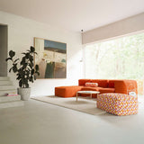 Dreisitziges Soft Sofa Indoor von sackit in warmem Orange mit integrierter Chaiselongue und gemustertem Pouf in einem hellen Wohnzimmer