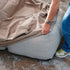 Wasserabweisende sandfarbene Schutzhülle wird über ein hellgraues Soft Sofa Outdoor gezogen und schützt den Lounger vor Wind und Wetter.
