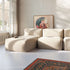 Beiges weiches modulares Sofa mit drei Sitzplätzen und großzügiger Liegefläche in einem hellen Wohnzimmer mit Fenster Kunst und Teppich