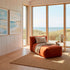 Weiches boneless Loungesofa in warmem Orange mit Kissen und Decke in hellem Holzinterieur mit Blick auf Dünen und Meer
