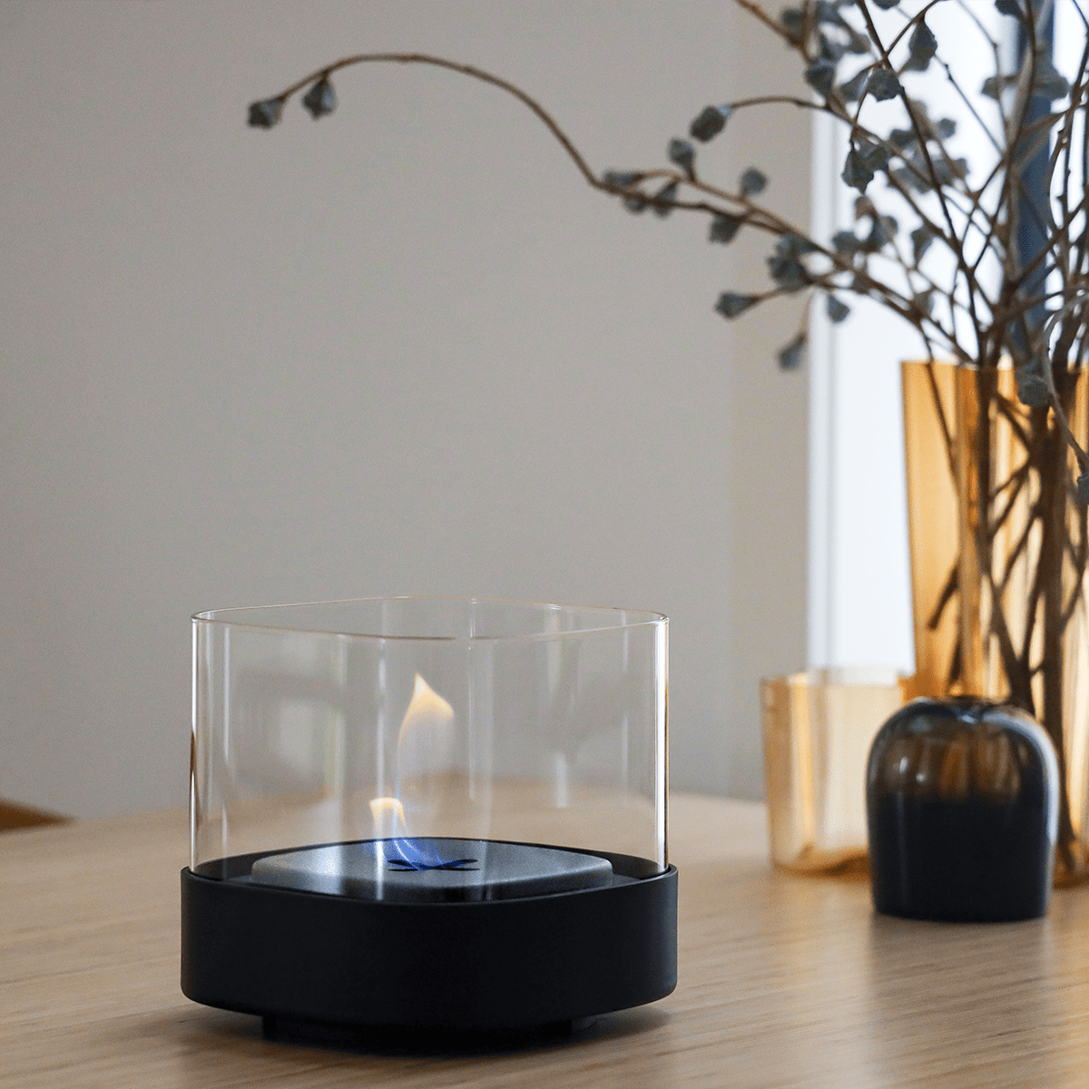 SACKit Bio Lamp Ø14 aus schwarzem pulverbeschichtetem Stahl mit hitzebeständigem Glas, draußen auf Holztisch. | Bio Lamp - Ø14 - | SACKit