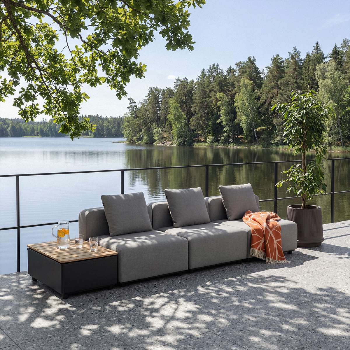 Graues modulares Outdoor Sofa auf einer Terrasse am See mit schwarzem Beistelltisch orangefarbener Decke und skandinavischem Design von sackit | Cobana Lounge Sofa - Seat - Kirra Indigo | SACKit