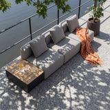Graues modulares Outdoor Lounge Sofa von sackit mit drei Sitzplätzen und passendem Beistelltisch auf einer sonnigen Terrasse mit Decke und Getränken | Cobana Lounge Sofa - 3 seater w/ Patio Storage Table - Kirra Sand Mit Armlehnen Mit Hocker | SACKit