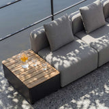 Graues modulares Outdoor Sofa von sackit mit zwei Sitzplätzen und Kissen neben einem Holz Beistelltisch auf einer Terrasse im Schatten | Cobana Lounge Sofa - 2 seater - Kirra Sand Ohne Armlehnen Mit Hocker | SACKit