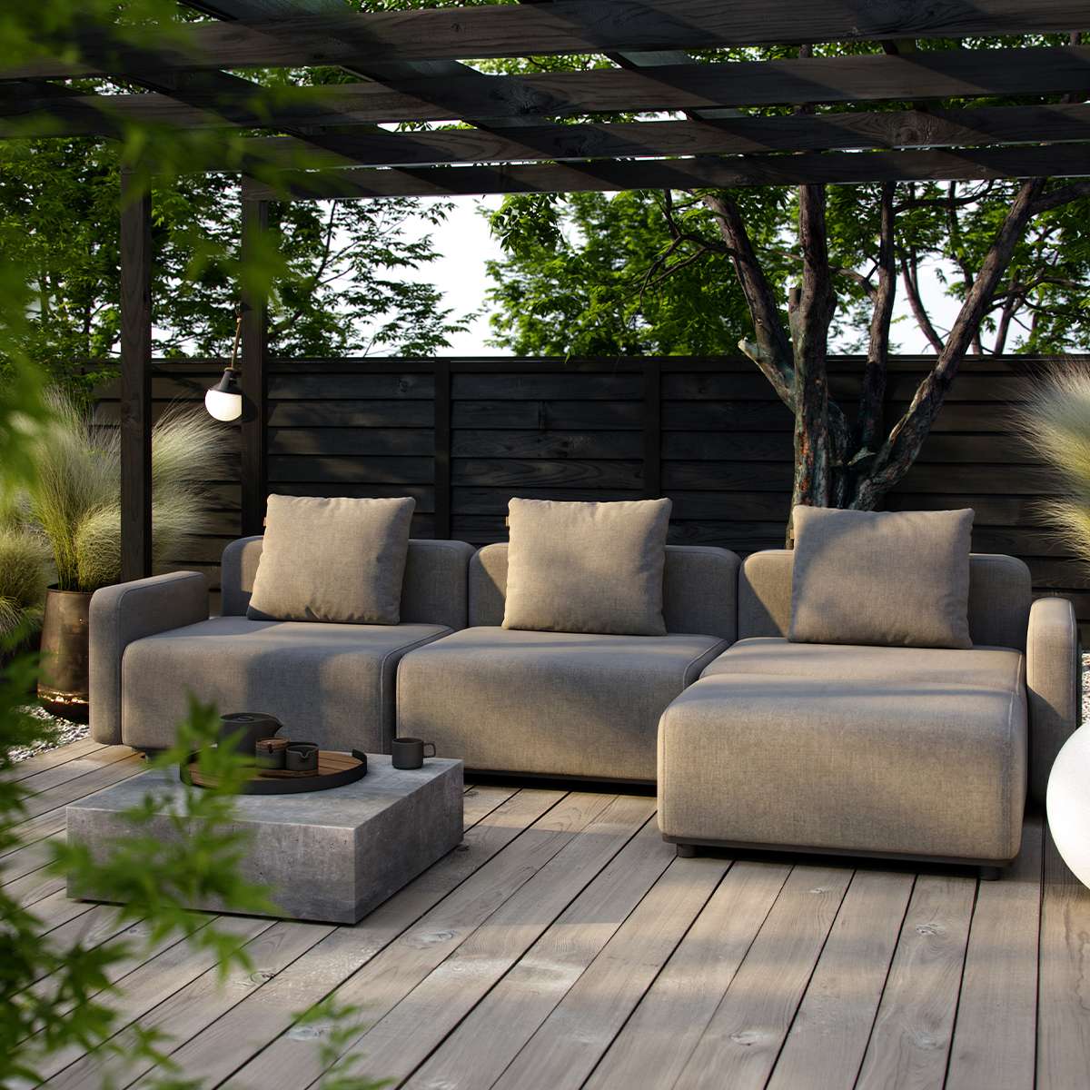 Graues modulares Outdoor Sofa von sackit mit drei Sitzplätzen und beigen Kissen auf einer Holzterrasse unter einer Pergola im grünen Garten | Cobana Lounge Sofa - 3 seater - Kirra Sand Mit Armlehnen Mit Hocker | SACKit