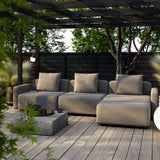 Graues modulares Outdoor Sofa von sackit mit drei Sitzplätzen und beigen Kissen auf einer Holzterrasse unter einer Pergola im grünen Garten | Cobana Lounge Sofa - 3 seater - Kirra Sand Mit Armlehnen Mit Hocker | SACKit