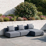 Graues modulares Cobana Lounge Sofa von sackit im Garten mit drei Sitzmodulen und Rückenkissen auf einer gepflasterten Terrasse | Cobana Lounge Sofa - 3 seater - Kirra Sand Mit Armlehnen Mit Hocker | SACKit