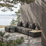 Modulares Outdoor Sofa von sackit auf einer Holzterrasse am Wasser mit dunklen Polstern und Beistelltisch zwischen Kiefern im skandinavischen Stil | Cobana Lounge Sofa - 3 seater w/ Patio Storage Table - Kirra Sand Mit Armlehnen Mit Hocker | SACKit