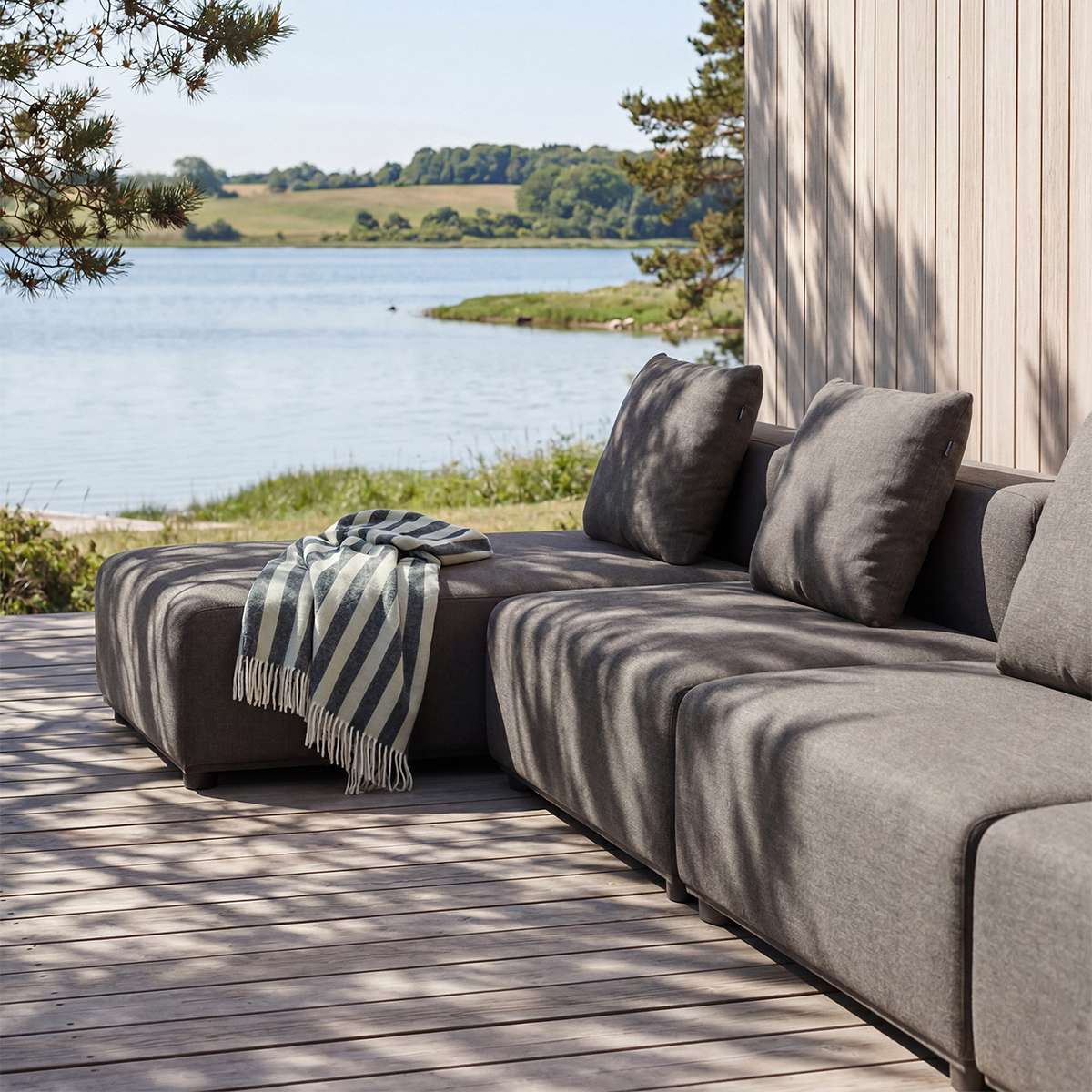 Graues sackit Cobana Outdoor Loungesofa mit dreisitzigem Sofa und Chaiselongue auf einer Holzterrasse am Wasser unter schattenspendenden Bäumen | Cobana Lounge Sofa - 3 Seater Chaise - Kirra Sand Mit Armlehnen | SACKit