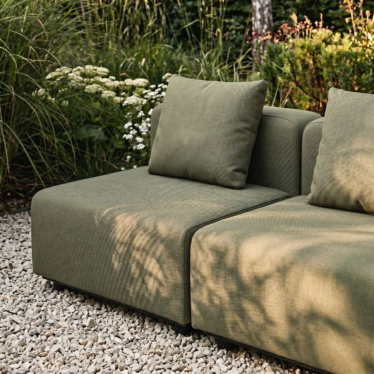 Grünes modulares Outdoor Sofa mit zwei Sitzplätzen und Kissen auf hellem Kies in einem üppigen Garten gestaltet in Dänemark für nordisches Wetter | Cobana Lounge Sofa - 4 seater corner sofa - Kirra Sand Mit Armlehnen | SACKit