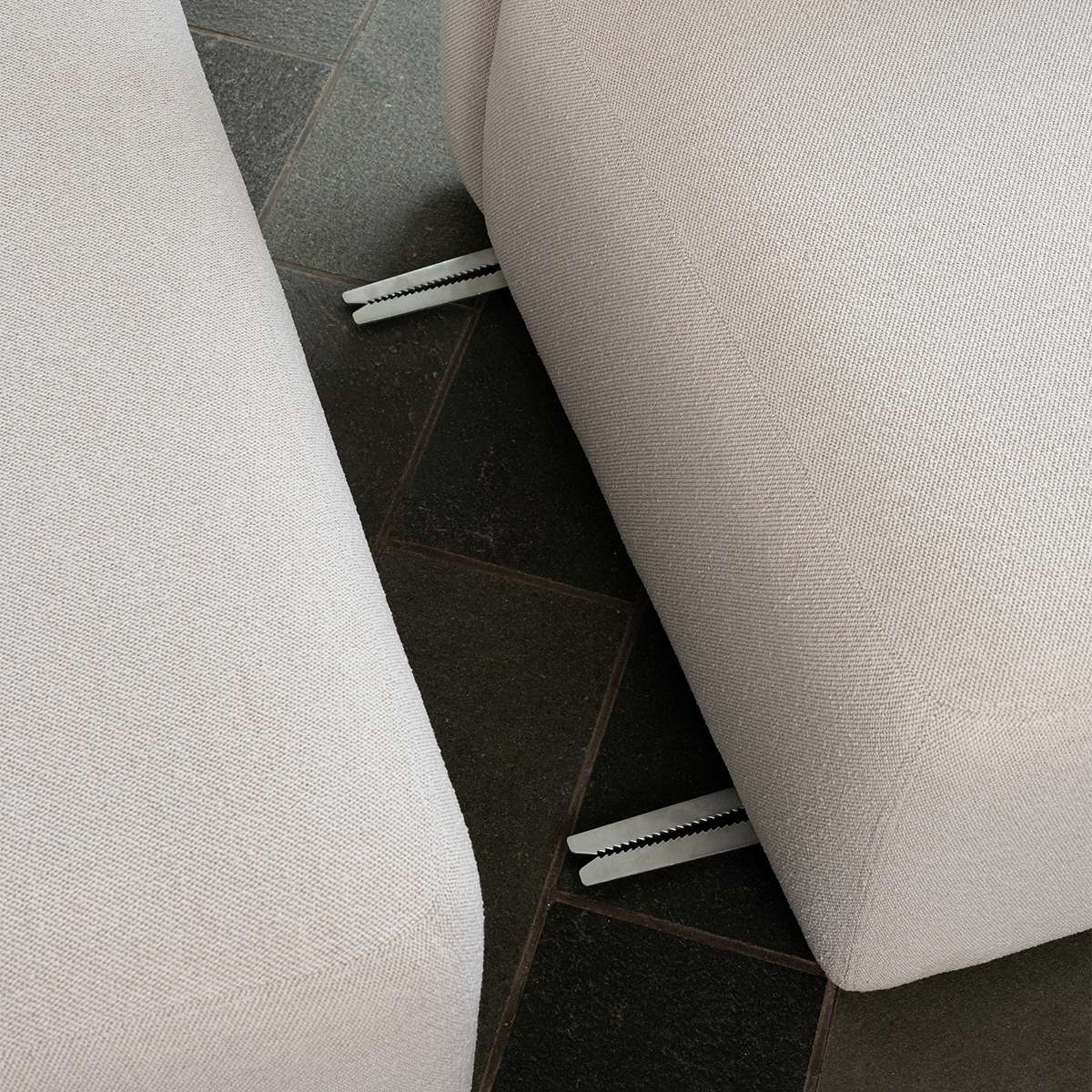 Nahaufnahme eines hellen skandinavischen Sofas mit sichtbaren Metallverbindern zwischen den gepolsterten Segmenten auf dunklem Fliesenboden | Fjord Sofa - Chaise Left - Cosmo Clay | SACKit