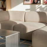 Beigefarbenes dreisitziges Sofa mit rechter Chaise und weichen Rundungen in einem hellen skandinavischen Wohnzimmer mit Kunst und Couchtisch