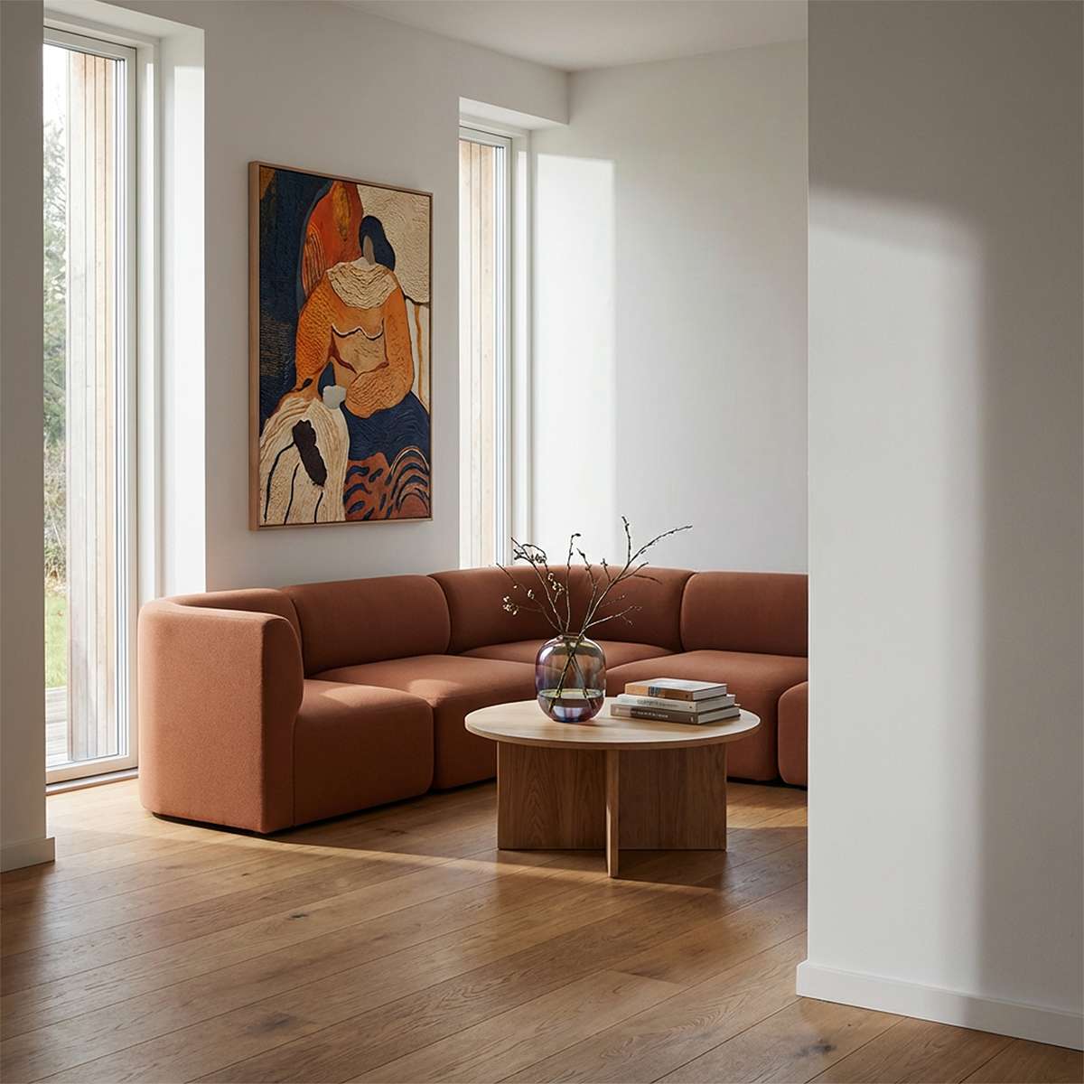 Braunes Fjord Ecksofa von sackit in einem hellen skandinavischen Wohnzimmer mit Holzboden rundem Couchtisch und abstrakter Wandkunst | Fjord Sofa - Corner Sofa - Cosmo Terracotta | SACKit