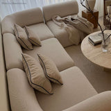 Beiges skandinavisches Ecksofa von sackit mit weichen Polstern und Kissen neben einem runden Couchtisch in einem stilvoll eingerichteten Wohnzimmer | Fjord Sofa - Corner Section Left - Cosmo Clay | SACKit