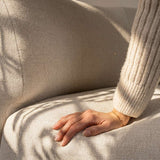 Nahaufnahme des hellbeigen Stoffbezugs eines Fjord Sofas mit einer Hand auf der weichen Sitzfläche im warmen Sonnenlicht | Fjord Sofa - Corner Sofa w/ open end - Cosmo Terracotta | SACKit