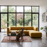 Senfgelbes skandinavisches Sofa mit Ottomane in einem hellen Wohnzimmer vor großen Fenstern, mit Hund auf einem gemusterten Teppich | Fjord Sofa - 3 seater - Cosmo Olive Mit Hocker | SACKit