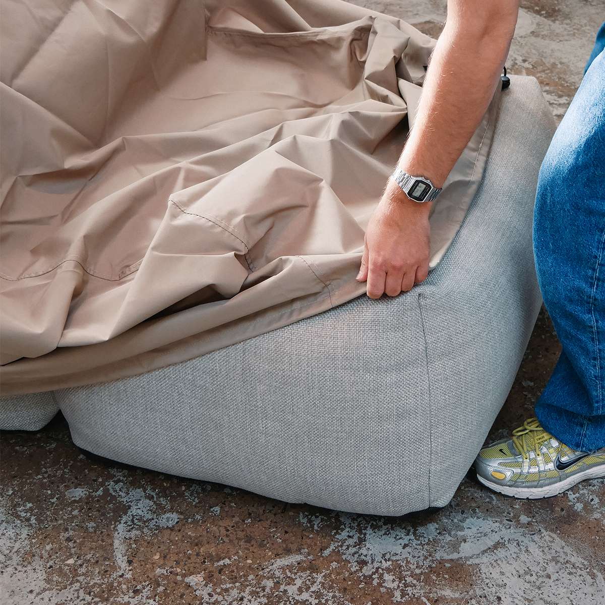 Wasserabweisende sandfarbene Schutzhülle wird über ein hellgraues Soft Sofa Outdoor gezogen und schützt den Lounger vor Wind und Wetter.